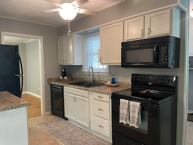 Kitchen with black appliances, crown molding, white cabinets, ceiling fan, and light countertops