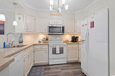 Kitchen featuring white appliances, white cabinets, tasteful backsplash, ornamental molding, and decorative light fixtures