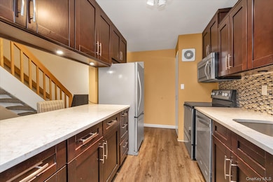 Kitchen with stainless steel appliances, light stone countertops, light wood-style floors, and decorative backsplash