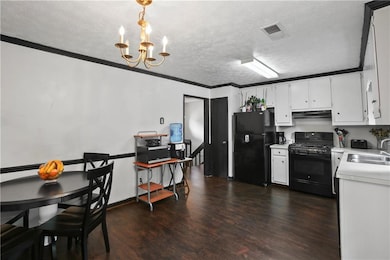 Kitchen with black appliances, under cabinet range hood, light countertops, dark wood finished floors, and a chandelier
