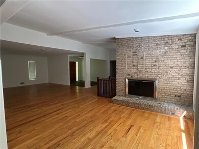 Unfurnished living room featuring hardwood floors, beam ceiling, and a brick fireplace