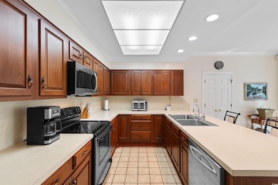 Kitchen with ornamental molding, appliances with stainless steel finishes, recessed lighting, light countertops, and a peninsula
