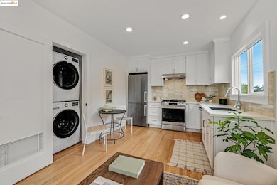 Kitchen with light wood finished floors, stainless steel appliances, white cabinetry, recessed lighting, and stacked washing machine and dryer