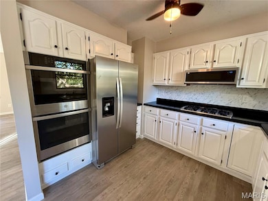 Kitchen with dark countertops, appliances with stainless steel finishes, white cabinetry, decorative backsplash, and light wood-style flooring