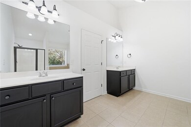 Full bath with two vanities, a shower stall, and light tile patterned flooring