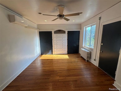 Unfurnished bedroom featuring multiple closets, dark wood-type flooring, radiator, ceiling fan, and an AC wall unit