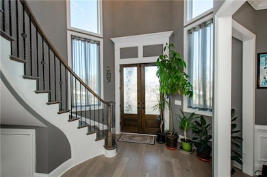 Entrance foyer with french doors, stairway, a high ceiling, wood finished floors, and plenty of natural light
