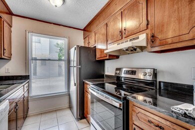 Kitchen with electric stove, under cabinet range hood, brown cabinets, dark countertops, and ornamental molding