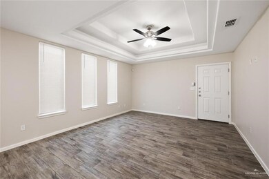 Unfurnished room with a tray ceiling, a ceiling fan, dark wood-type flooring, and baseboards
