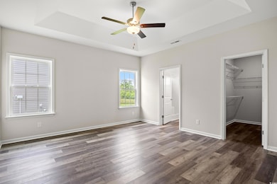 Unfurnished bedroom with a tray ceiling, a spacious closet, dark wood finished floors, and a closet