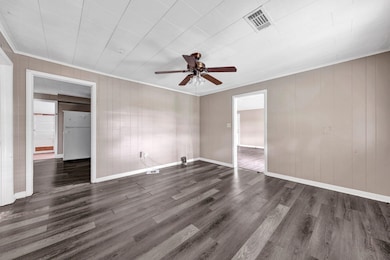 Empty room featuring crown molding, a ceiling fan, dark wood-style floors, and wooden walls