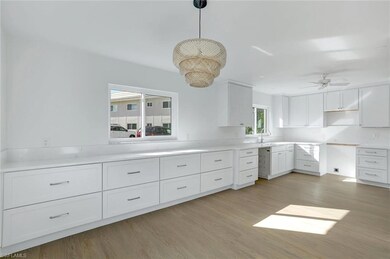 Kitchen featuring light wood-type flooring, white cabinets, hanging light fixtures, a ceiling fan, and a sink