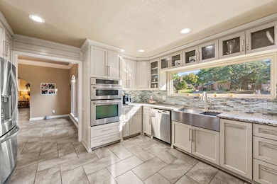 Kitchen featuring stainless steel appliances, arched walkways, backsplash, light stone counters, and crown molding