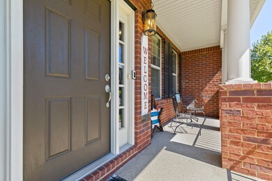 This is the perfect place to relax and enjoy your favorite beverage on a hot day.  Notice the columns with a brick base, Ring doorbell, and a lantern-style light fixture.