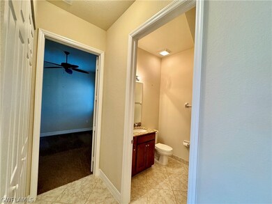 Hallway to bedroom and bathroom with tile patterned floors, toilet, vanity, and ceiling fan