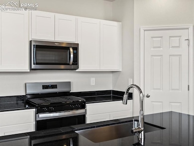 Kitchen featuring appliances with stainless steel finishes, dark stone counters, and white cabinets
