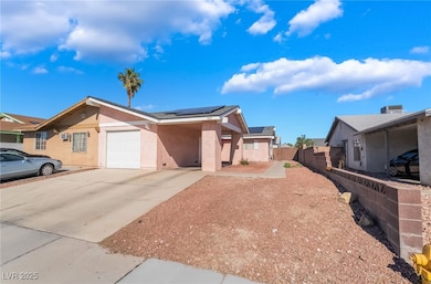 View of front facade with stucco siding, driveway, and roof mounted solar panels