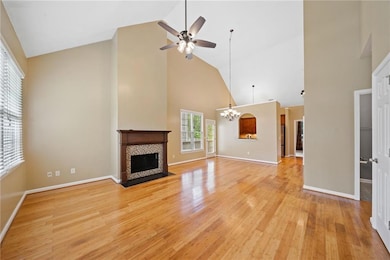 Unfurnished living room with high vaulted ceiling, a chandelier, a ceiling fan, a tiled fireplace, and light wood-style floors