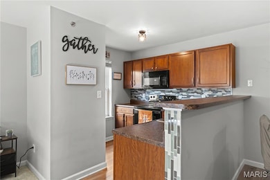 Kitchen featuring dark countertops, decorative backsplash, black appliances, brown cabinetry, and a peninsula