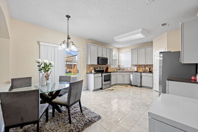 Kitchen featuring backsplash, stainless steel appliances, a textured ceiling, pendant lighting, and a chandelier
