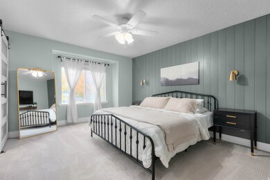 Bedroom with carpet flooring, a textured ceiling, a barn door, a ceiling fan, and wooden walls