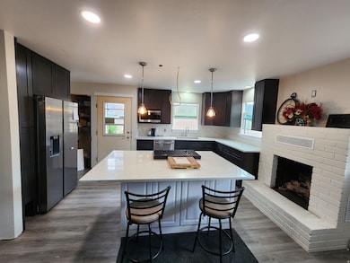 Kitchen with appliances with stainless steel finishes, decorative light fixtures, light stone countertops, a breakfast bar area, and dark wood finished floors