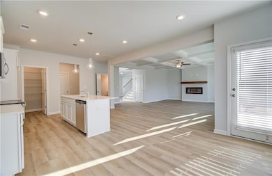 Kitchen with light hardwood / wood-style flooring, pendant lighting, a kitchen island with sink, white cabinetry, and coffered ceiling