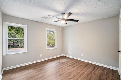 Empty room featuring a textured ceiling, a wealth of natural light, and dark wood-type flooring