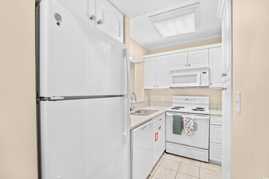 Kitchen featuring white appliances, white cabinets, light tile patterned floors, crown molding, and light stone countertops