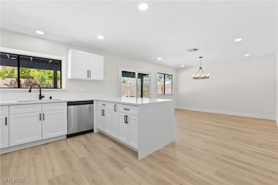 Kitchen with a peninsula, recessed lighting, white cabinetry, stainless steel dishwasher, and light stone counters