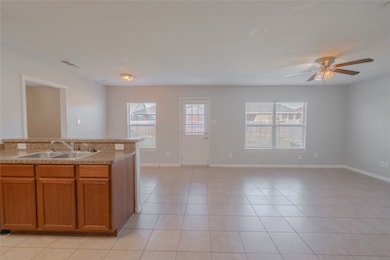 Kitchen featuring brown cabinetry, light countertops, light tile patterned floors, a ceiling fan, and open floor plan