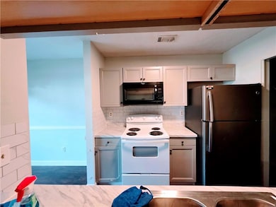 Kitchen featuring white electric range, freestanding refrigerator, black microwave, tasteful backsplash, and white cabinets