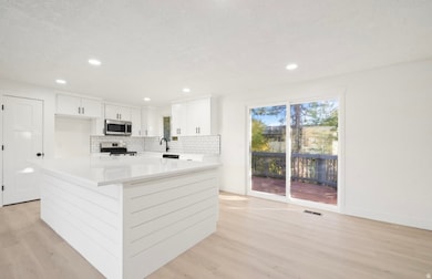 Kitchen with a kitchen island, white cabinetry, tasteful backsplash, stainless steel appliances, and light wood-style floors