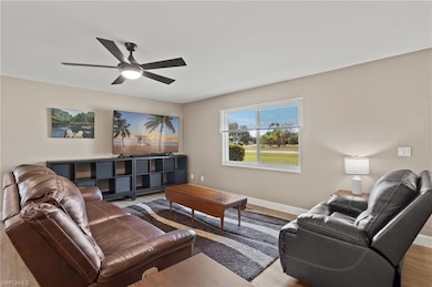 Natural light pours into the living room through the impact window with white blinds, illuminating the space and framing a serene view of greenery.