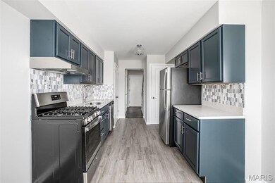 Kitchen with appliances with stainless steel finishes, a sink, under cabinet range hood, light countertops, and decorative backsplash