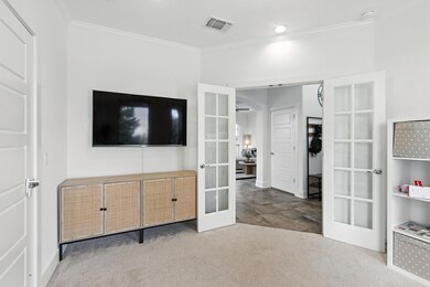 Carpeted bedroom with french doors and crown mold