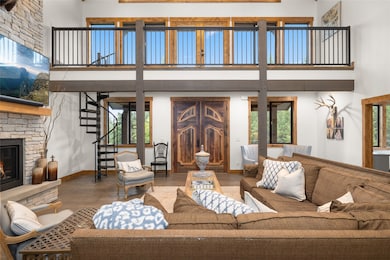 Living room featuring a high ceiling, a stone fireplace, wood finished floors, and stairway