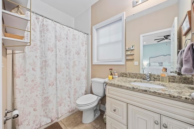 Ensuite bathroom with vanity, toilet, tile patterned floors, ceiling fan, and a shower with shower curtain