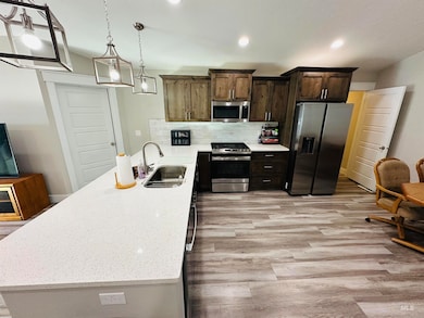 Kitchen with appliances with stainless steel finishes, backsplash, a peninsula, light stone countertops, and dark brown cabinets
