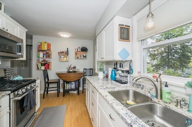 Kitchen featuring stainless steel appliances, white cabinetry, light wood-style floors, and light stone counters