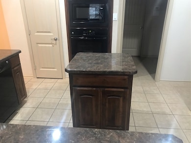 Kitchen featuring oven, light tile patterned floors, dishwashing machine, dark stone countertops, and dark brown cabinetry