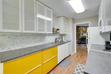 Kitchen with tasteful backsplash, light wood finished floors, a textured ceiling, black / electric stove, and white dishwasher