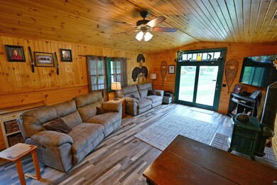 Living area featuring vaulted ceiling, wooden walls, ceiling fan, healthy amount of natural light, and wood finished floors