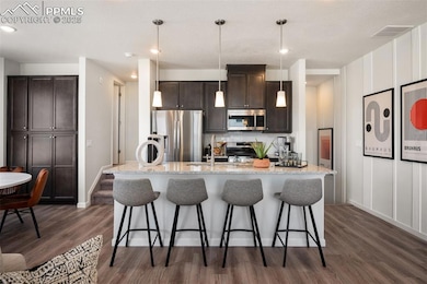 Kitchen featuring appliances with stainless steel finishes, dark brown cabinetry, a sink, dark wood-type flooring, and a breakfast bar