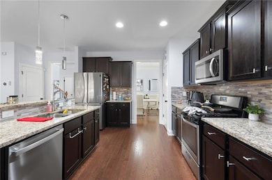 Kitchen featuring stainless steel appliances, a sink, decorative backsplash, dark wood-style flooring, and dark brown cabinetry