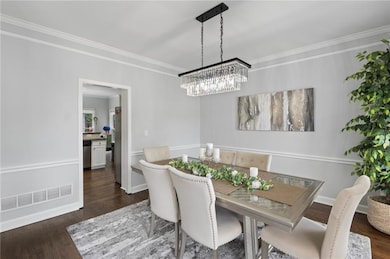Dining room with dark wood-style floors, crown molding, and a chandelier