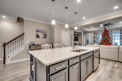 Kitchen with ornamental molding, light wood-type flooring, open floor plan, a center island with sink, and decorative light fixtures