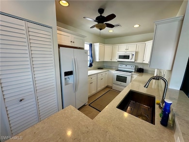 Kitchen with white appliances, white cabinetry, light stone counters, recessed lighting, and a ceiling fan