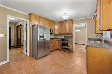 Kitchen featuring appliances with stainless steel finishes, backsplash, crown molding, light tile patterned floors, and dark countertops