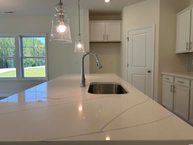 Kitchen with a sink, light stone counters, decorative backsplash, white cabinets, and decorative light fixtures